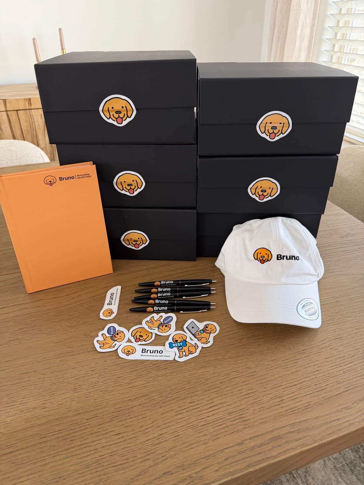 Stacked black Bruno swag boxes with a notebook, cap, pens and stickers laid out in front