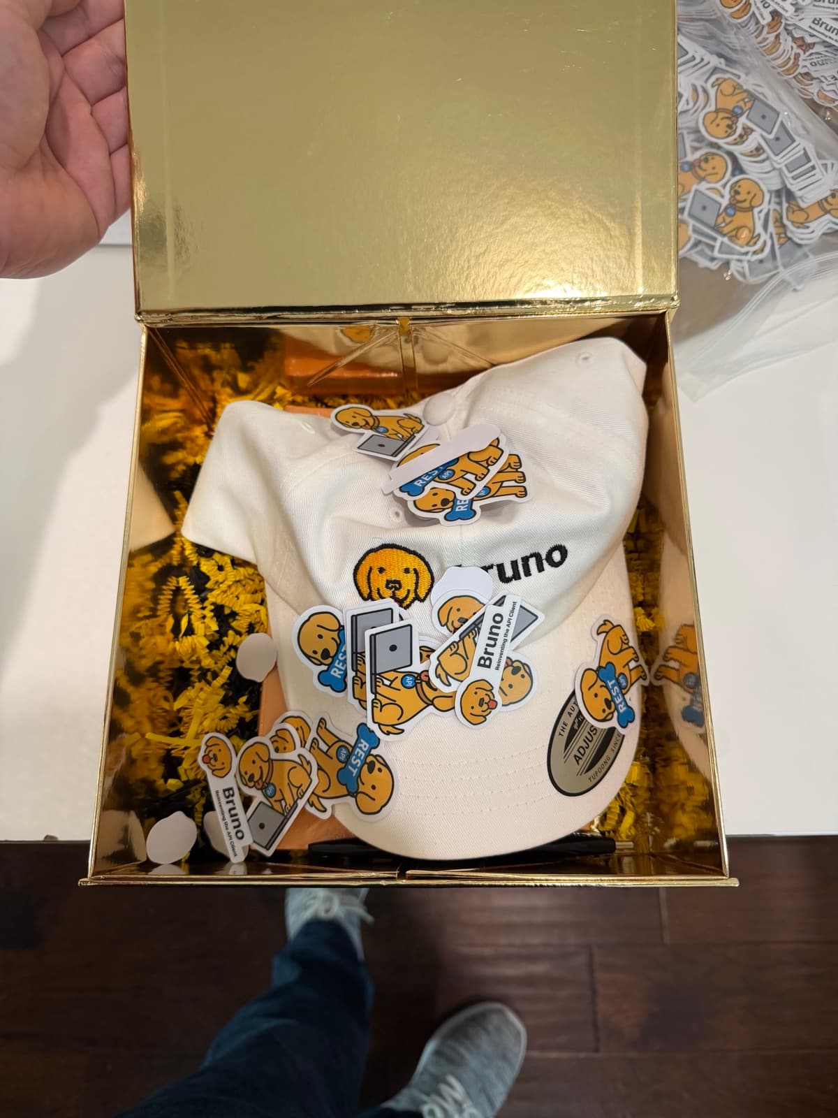 An open gold swag box holding a white Bruno cap and a pile of Bruno stickers